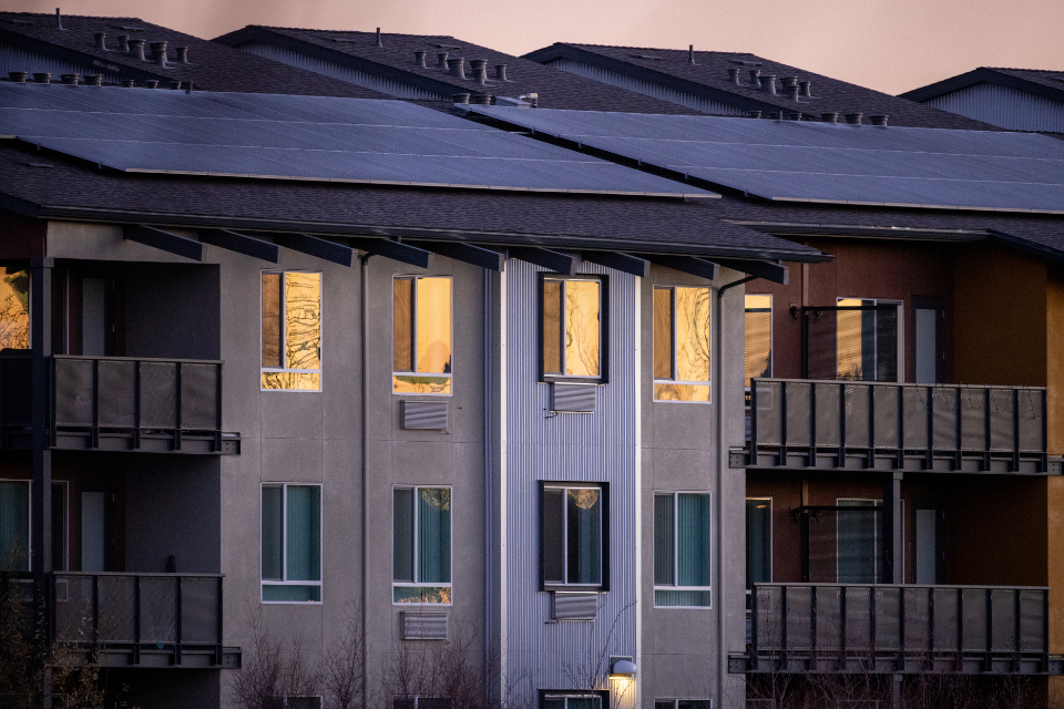 Solar panels cover the roofs of a row of apartment buildings at dusk
