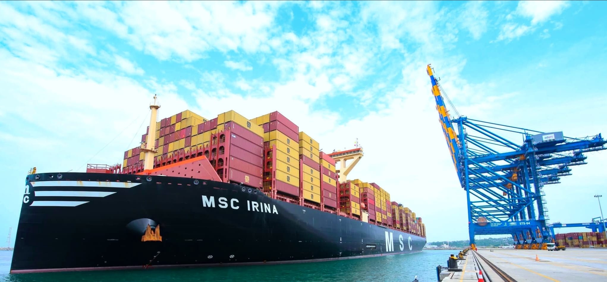 A large container ship stacked with shipping containers moored beside a blue gantry crane